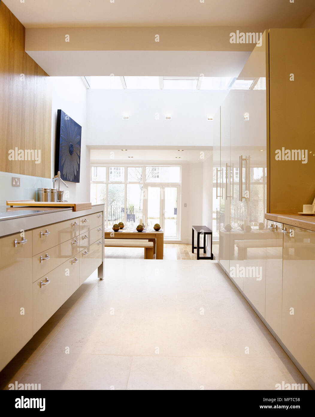 https://c8.alamy.com/comp/MFTC58/modern-kitchen-with-polished-cabinets-tile-floor-and-adjacent-dining-area-with-skylights-and-windows-MFTC58.jpg