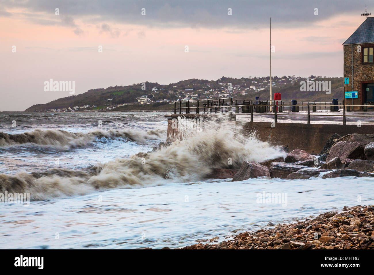 Waves breaking against the quay at Charmouth in Dorset at sunrise. Stock Photo
