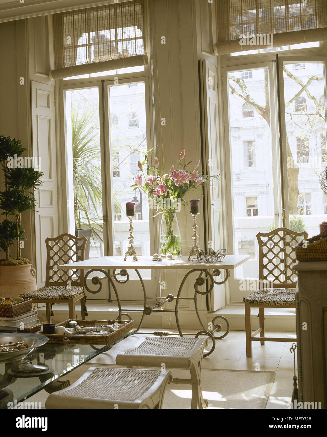 Wrought iron side table with flower arrangement in windows with shutters. Stock Photo