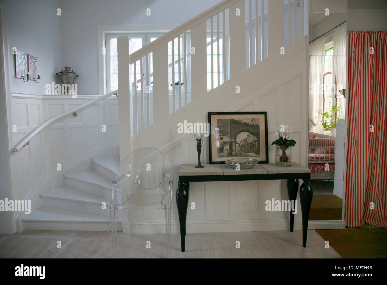 Philippe Starck Louis Ghost transparent chair next to side table in hallway with stairs Stock Photo