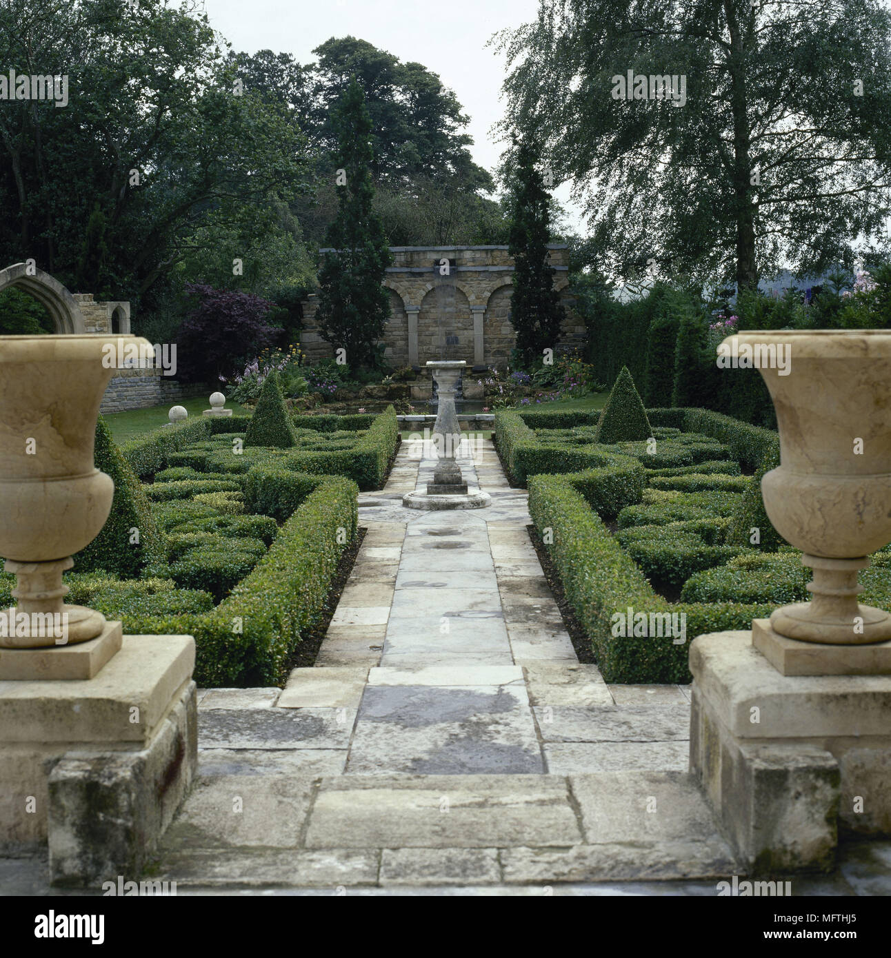 Formal garden stone urns, topiary, and a paved pathway through box hedging. Stock Photo