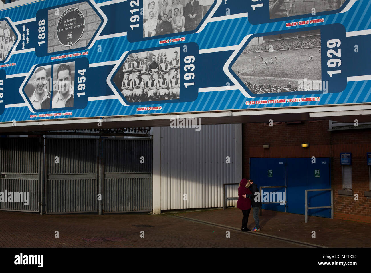 A couple kissing under a display dedicated to the home club's history before Blackburn Rovers played Shrewsbury Town in a Sky Bet League One fixture at Ewood Park. Both team were in the top three in the division at the start of the game. Blackburn won the match by 3 goals to 1, watched by a crowd of 13,579. Stock Photo