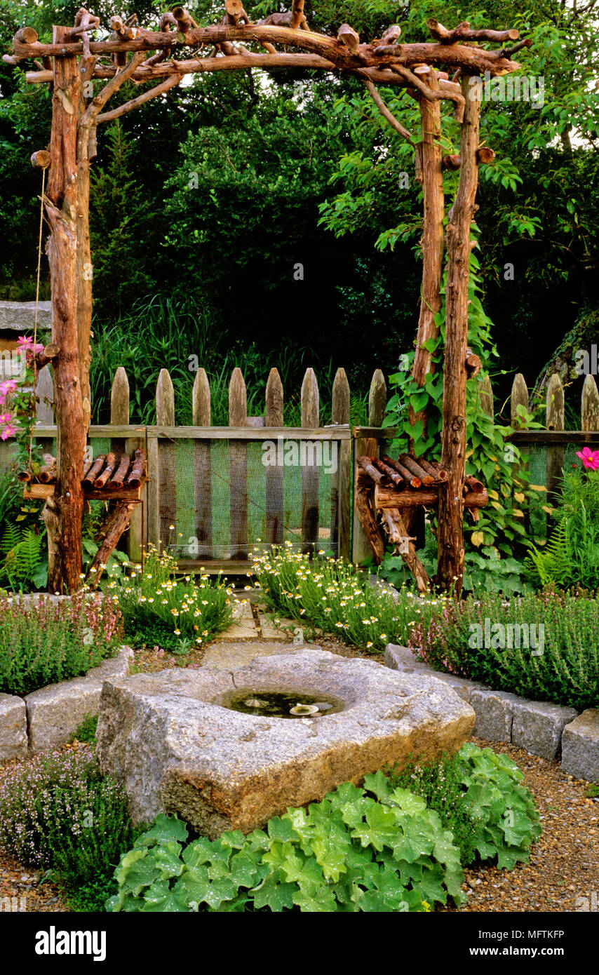 Garden arbour seat, stone water bowl and plantings of ALchemilla mollis, Thymus, Clematis 'Comtesse de Bouchaud', Ipomoea and Teucrium chamaedrys Stock Photo