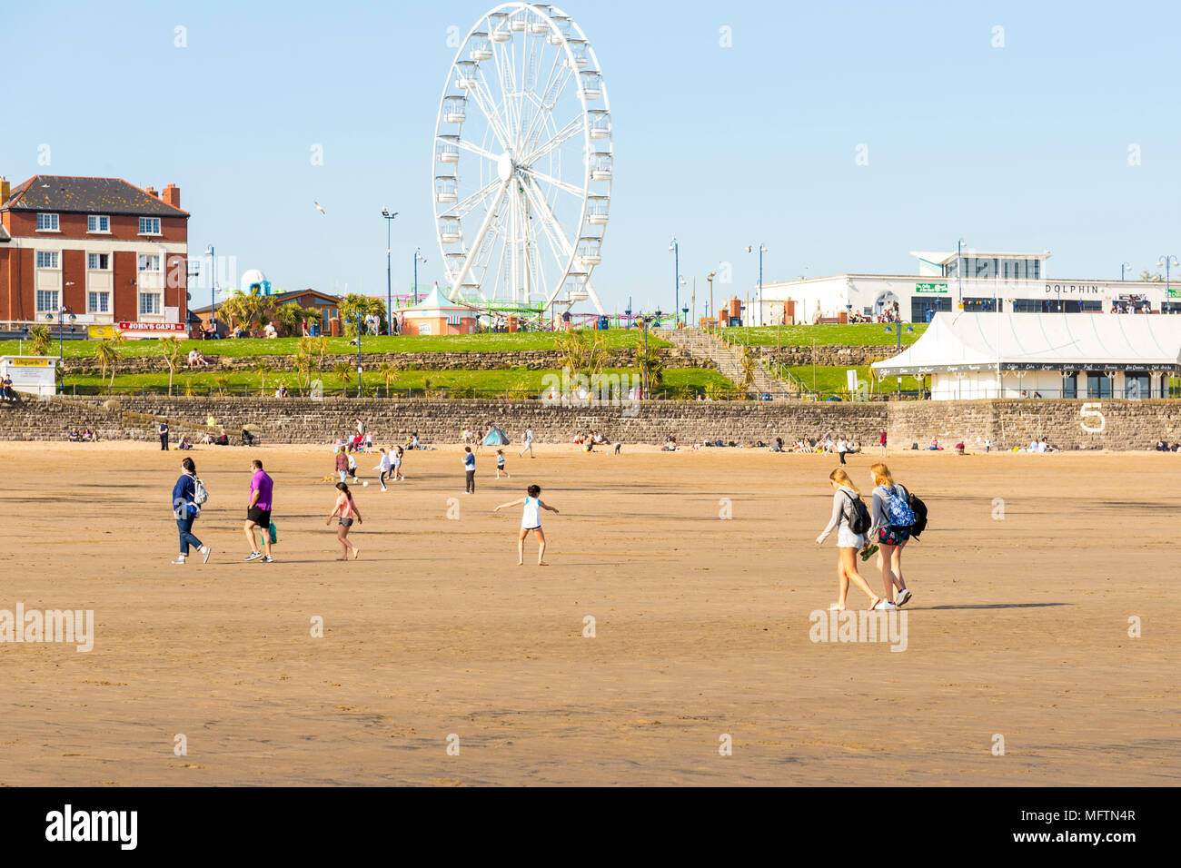 People enjoying a walk on the beach and sitting in the sun on a warm spring day at Barry Island, Wales Stock Photo