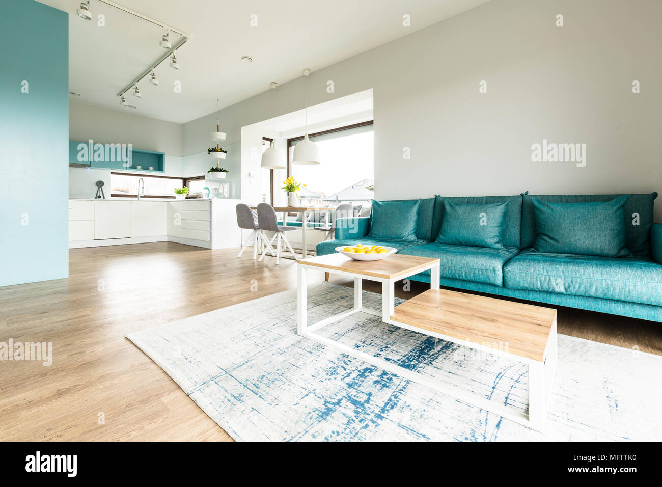 White and turquoise open space house interior with big sofa, modern kitchen  and a dining table by large windows Stock Photo - Alamy