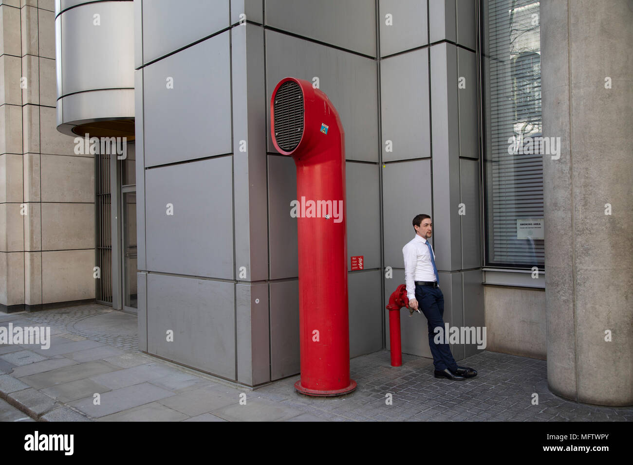 People interact with the red air ducts shaped like funnels, which are part of Vents 88 on London Wall by architect Richard Rogers, appear as strange architectural elements in the City of London, England, United Kingdom. 88 Wood Street is a commercial office tower development in the City of London, England. The architects were Richard Rogers Partnership, now known as Rogers Stirk Harbour + Partners. The building was constructed between 1993 and 2001 and was known as one of the Rogers buildings which placed normally concealed internal elements like ventilation ducts on the outside of the buildin Stock Photo