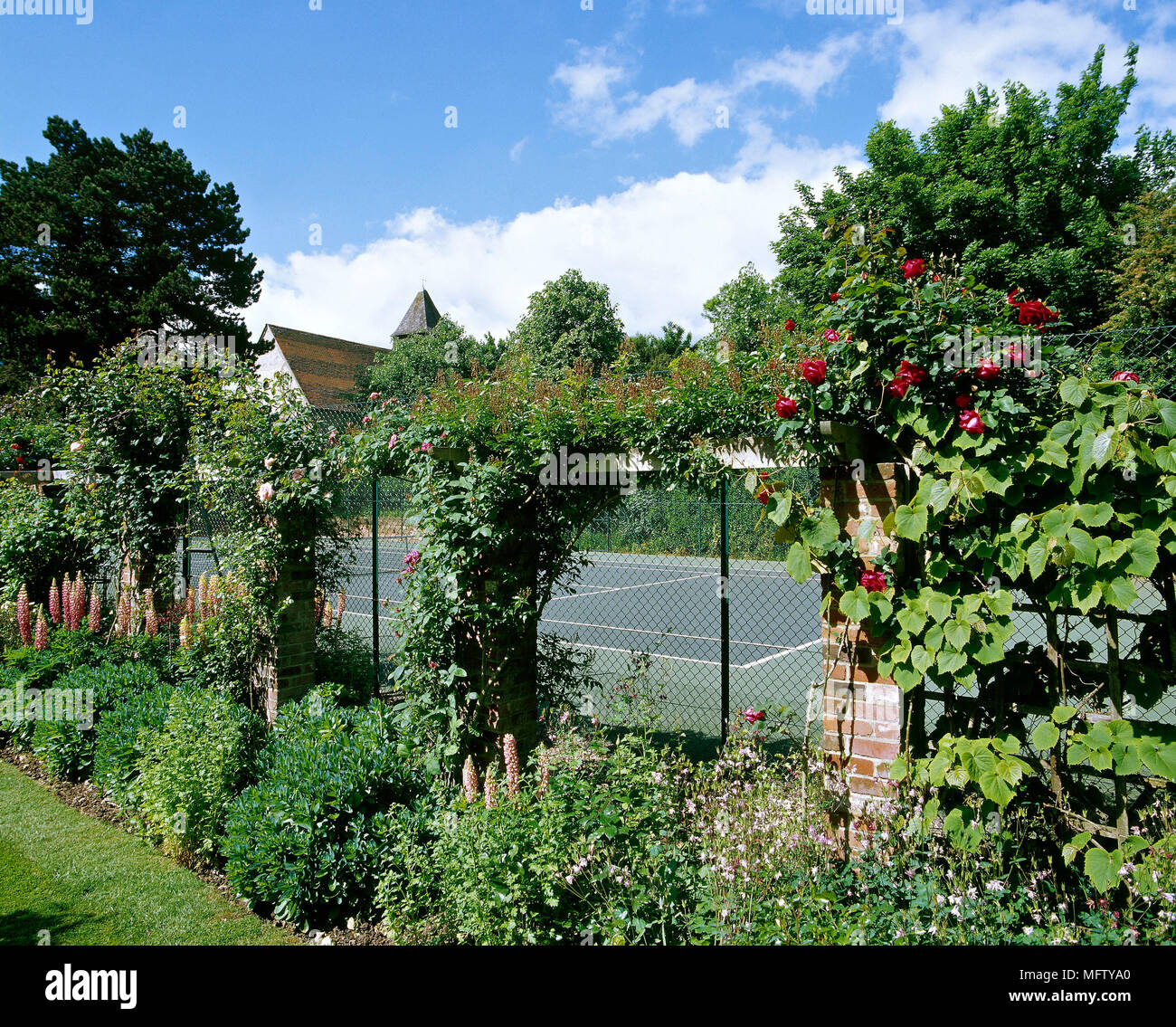 An outdoor tennis court surrounded by wire fencing, climbers and flower borders, Stock Photo