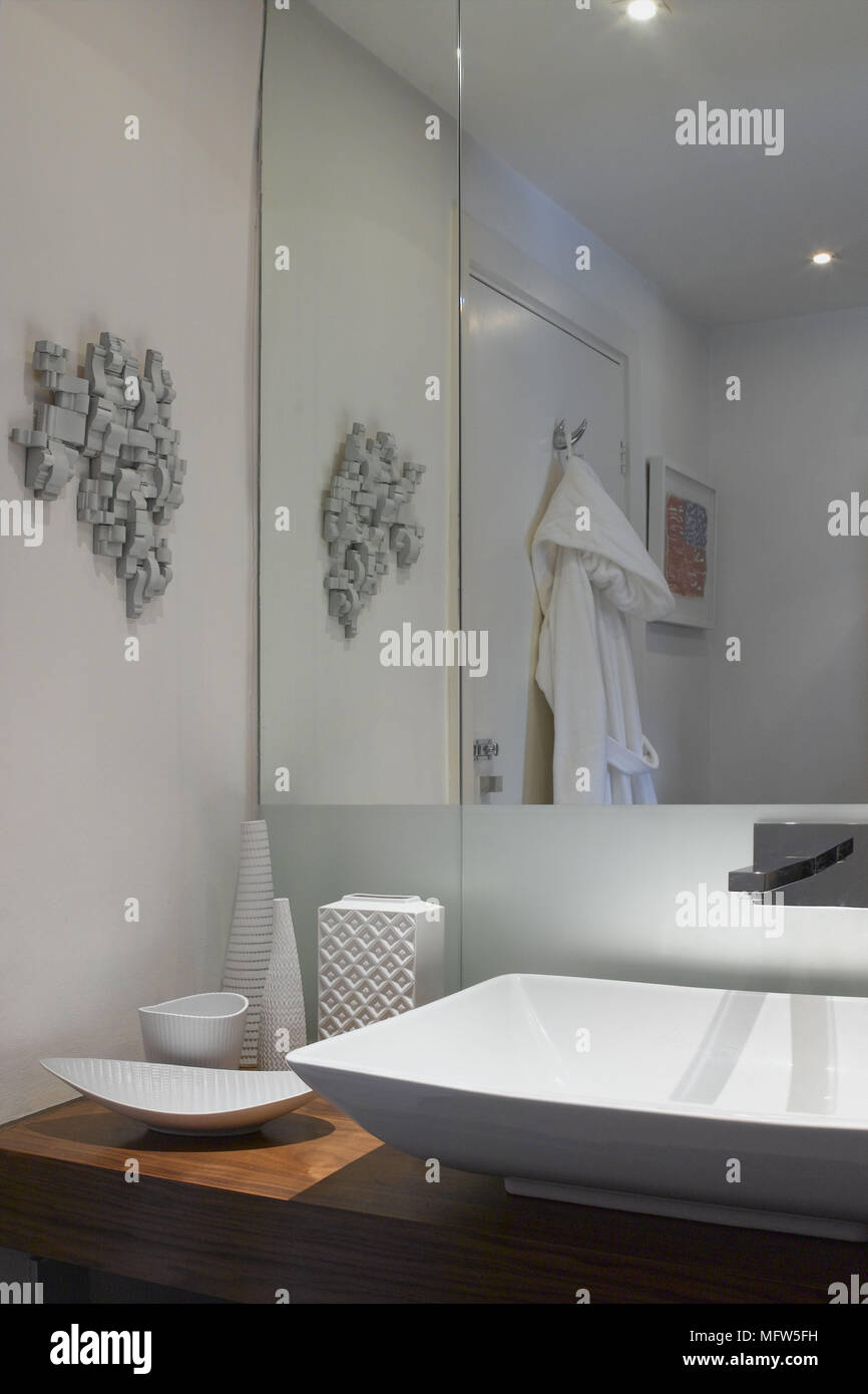 A detail of a modern bathroom washbasin set on wood unit white ceramic pieces mirror sense of space Stock Photo
