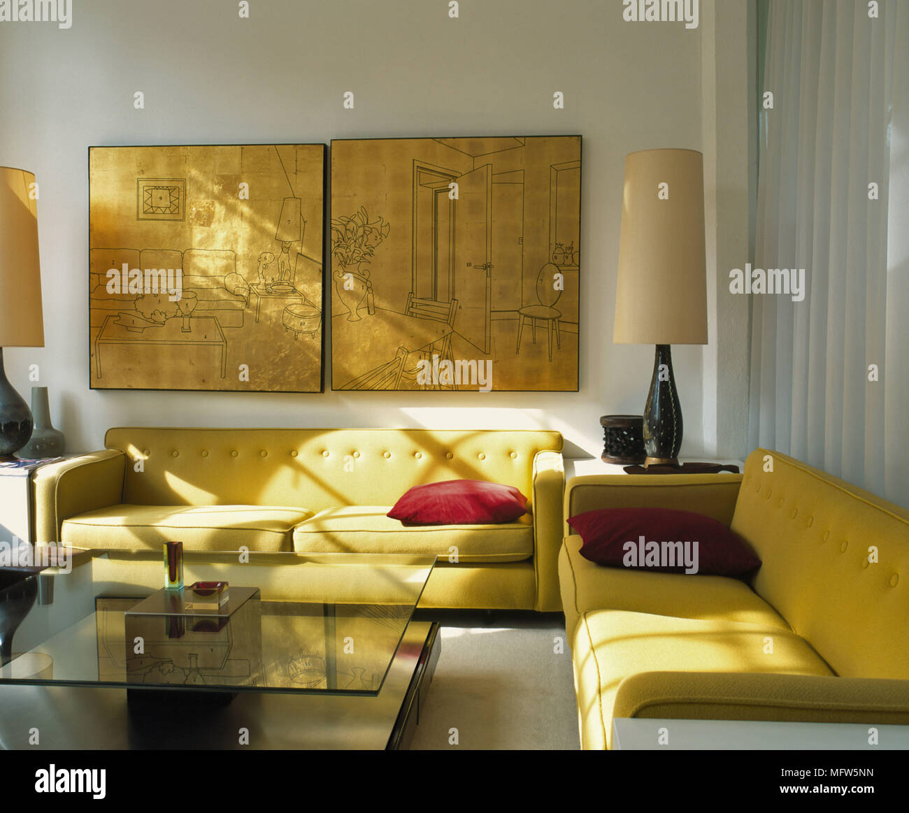A modern sitting room pair of yellow upholstered sofas glass coffee table lamps artwork Stock Photo