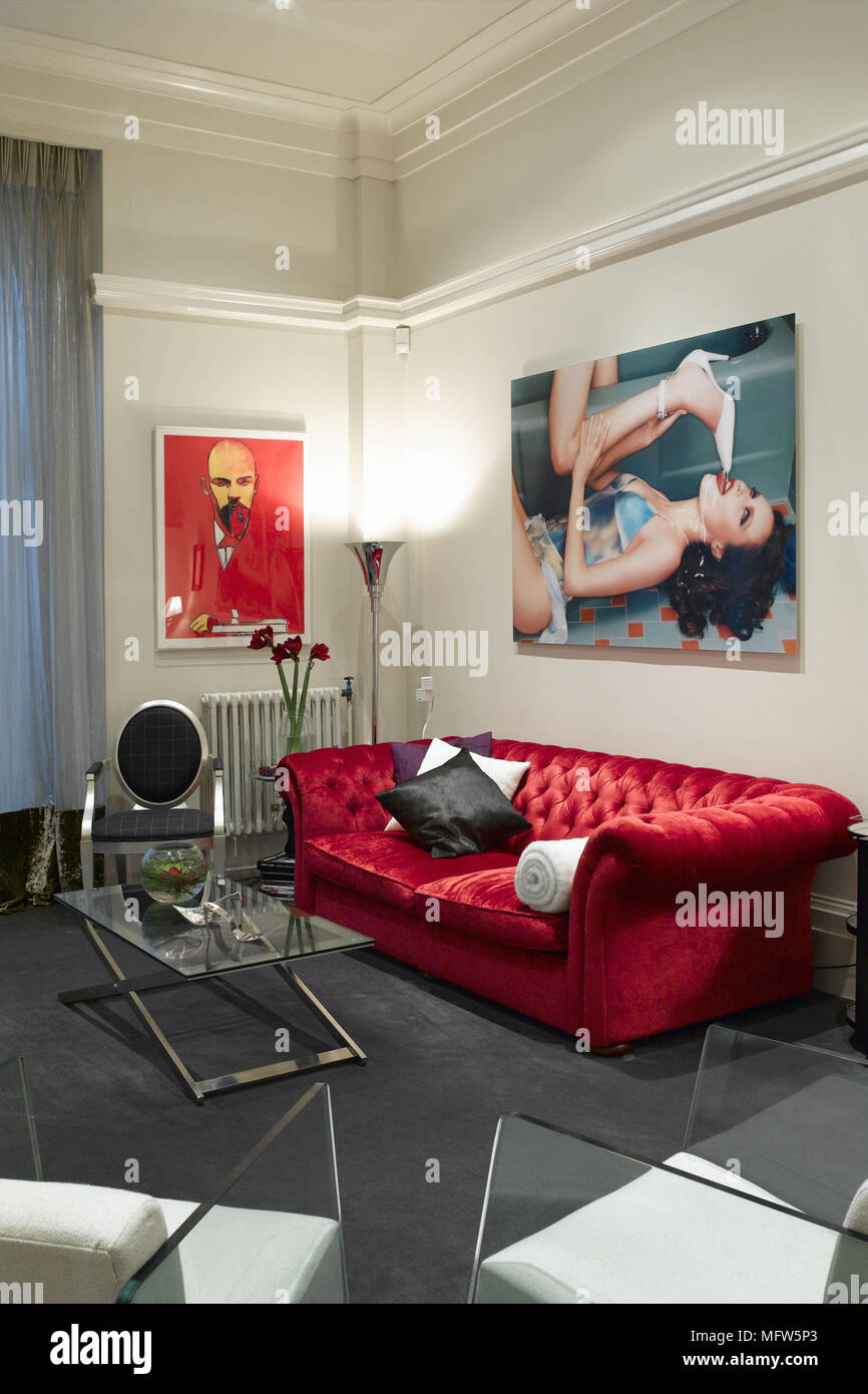 A modern sitting room with a red velvet sofa surrounded by two large pop art poster prints and in front of a glass coffee table. Stock Photo