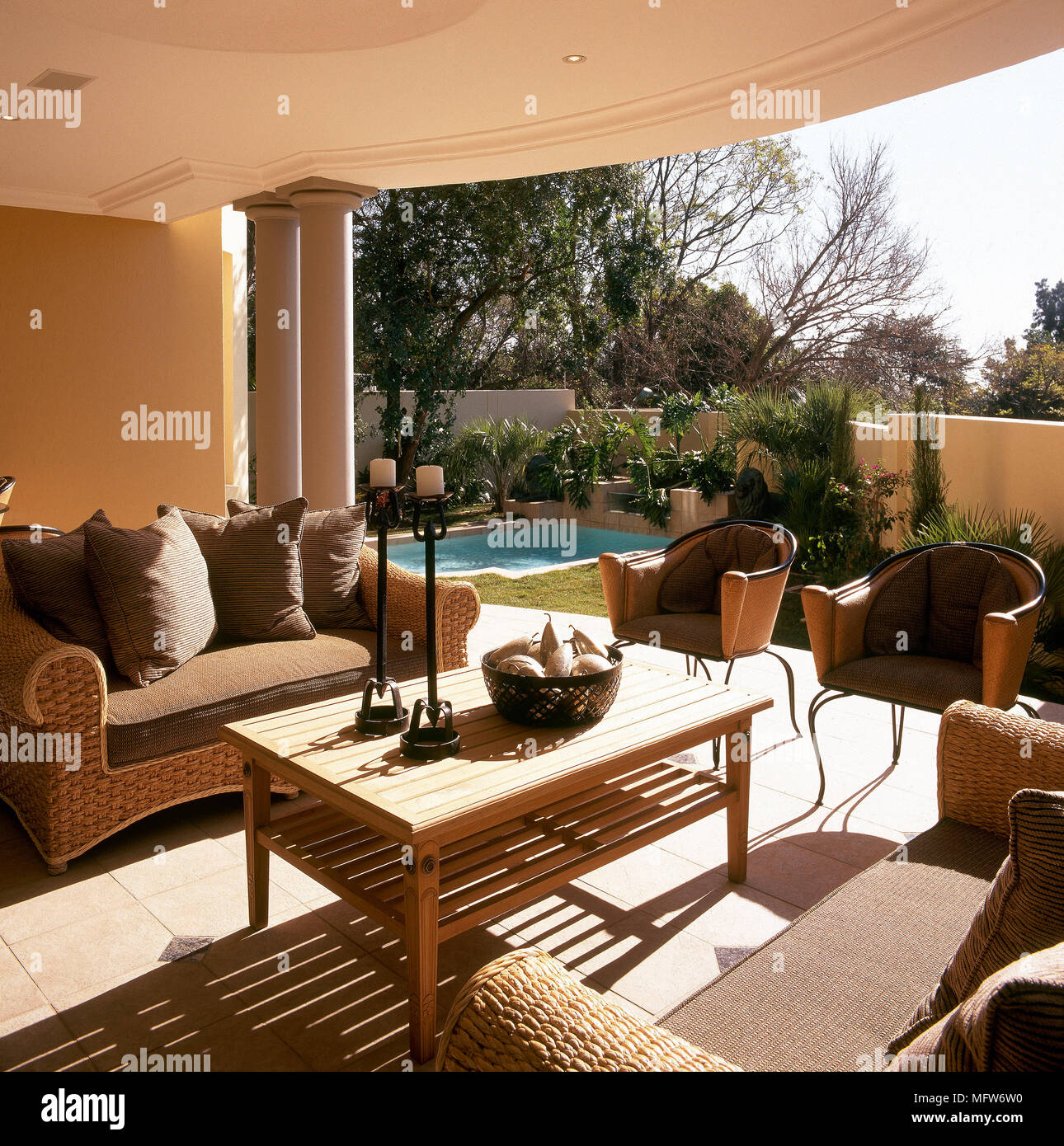 Tiled veranda with wicker seating arrangement, coffee table, and view of outdoor swimming pool and garden. Stock Photo