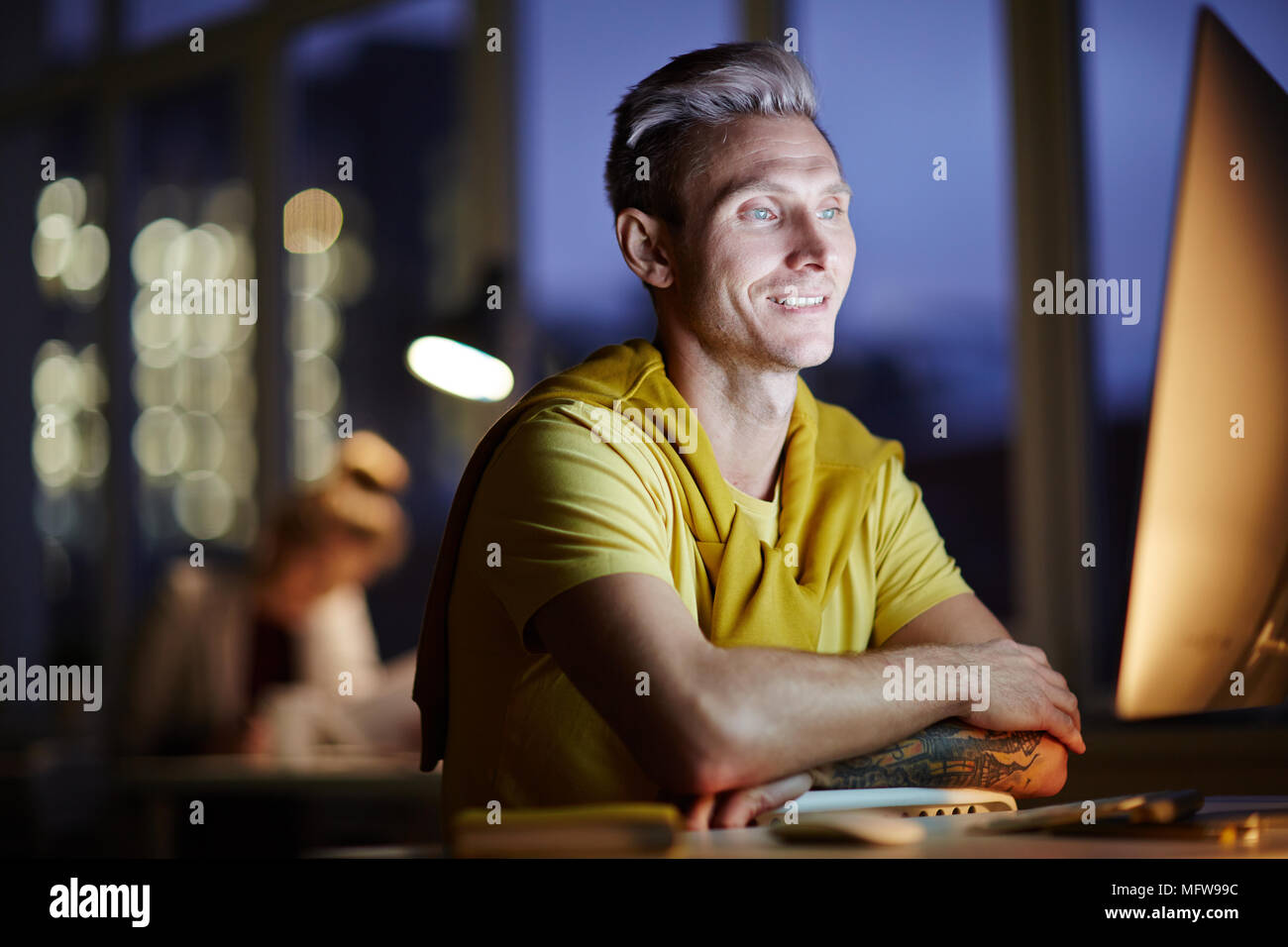 Young man working on computer at night in dark office. The designer works in the later time Stock Photo