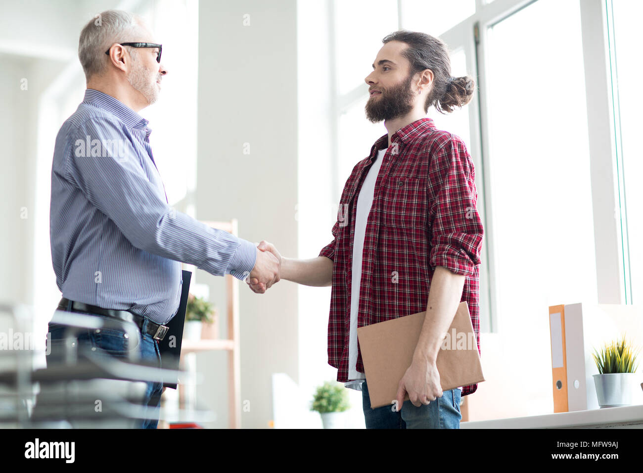Two business partners shaking hands at office. They are greeting to each other Stock Photo