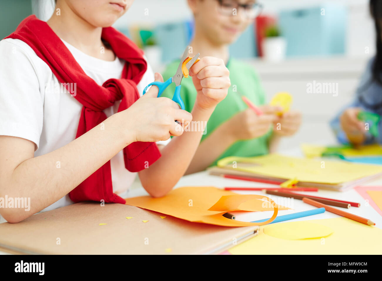 Kids sitting at school desk and cutting colorful paper with scissors