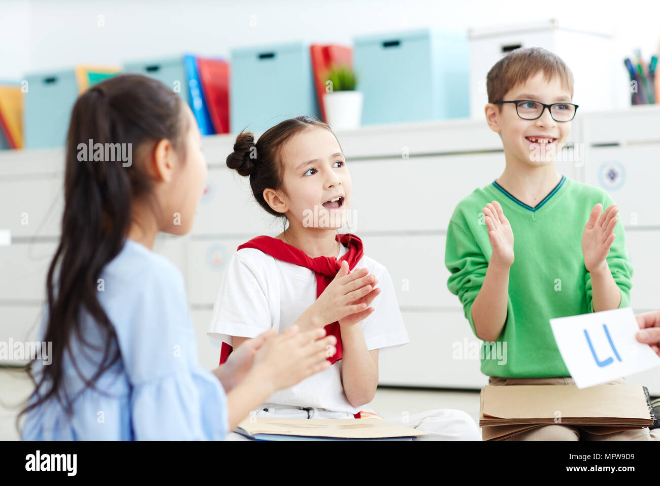 Group of elementary school kids singing songs and having fun while learning alphabet in classroom Stock Photo