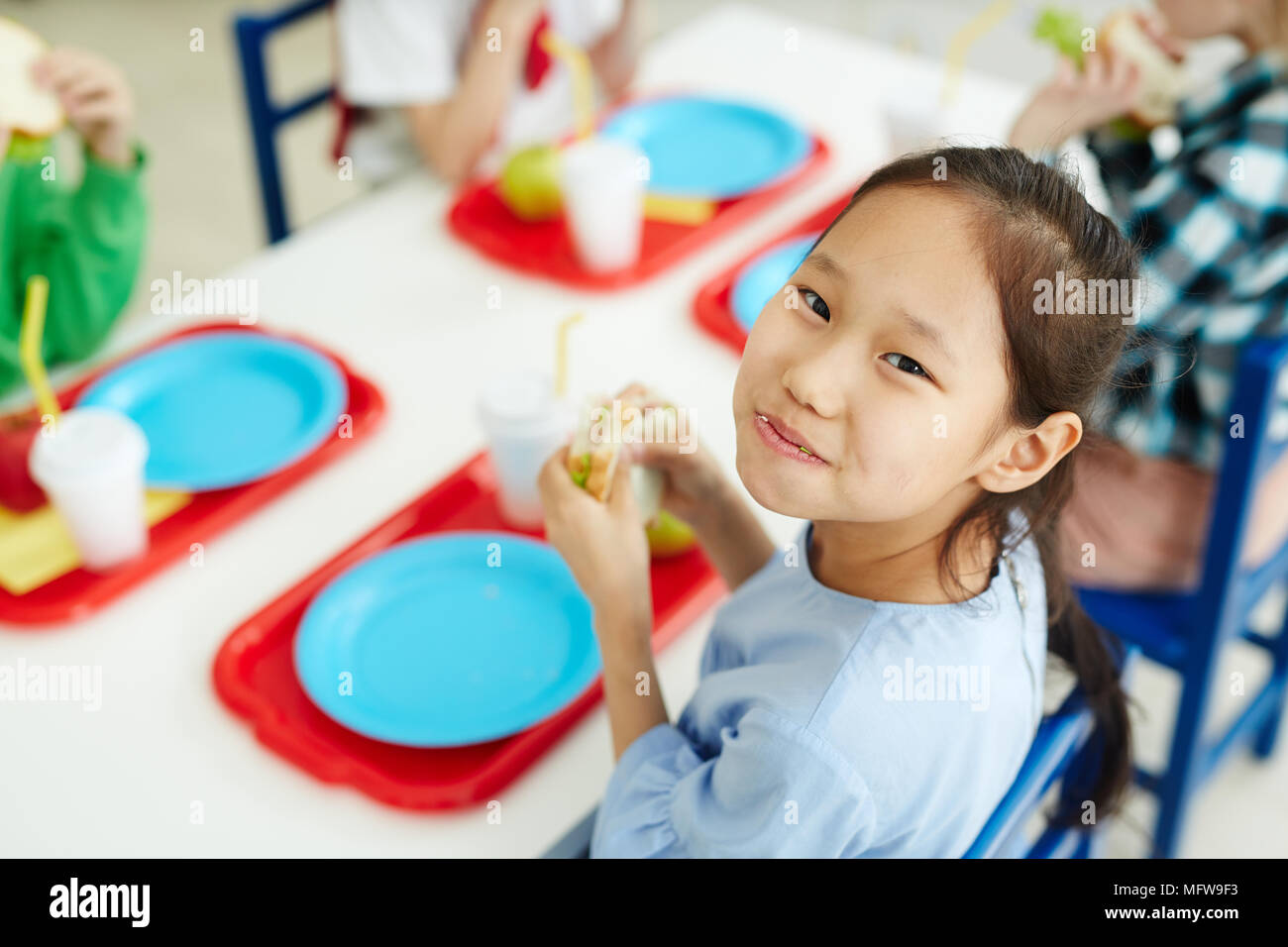 https://c8.alamy.com/comp/MFW9F3/pretty-asian-girl-sitting-at-table-with-classmates-in-primary-school-canteen-eating-sandwich-and-smiling-at-camera-cheerfully-MFW9F3.jpg
