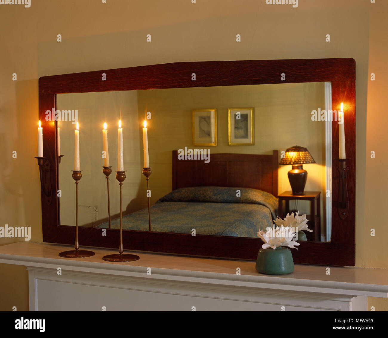 Double bed reflected in mirror above fireplace mantelpiece with lit