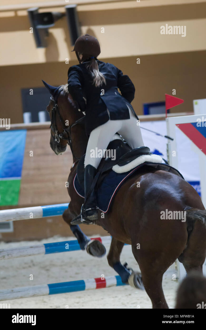 Young rider on black horse galloping at show jumping competition Stock
