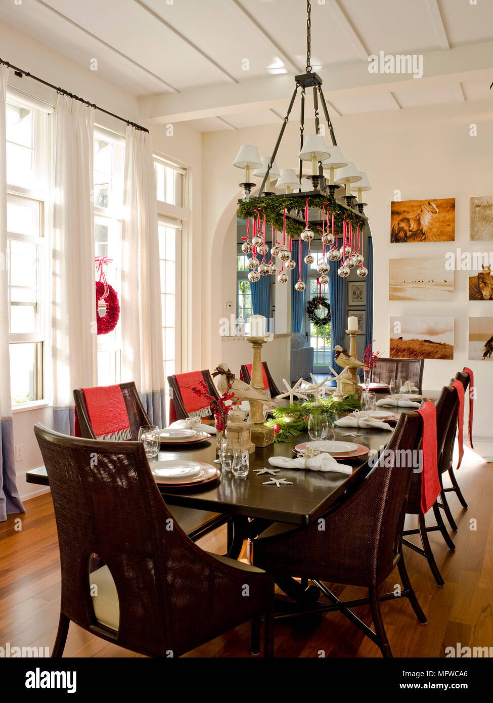 Christmas decorations hanging from chandelier above table laid for