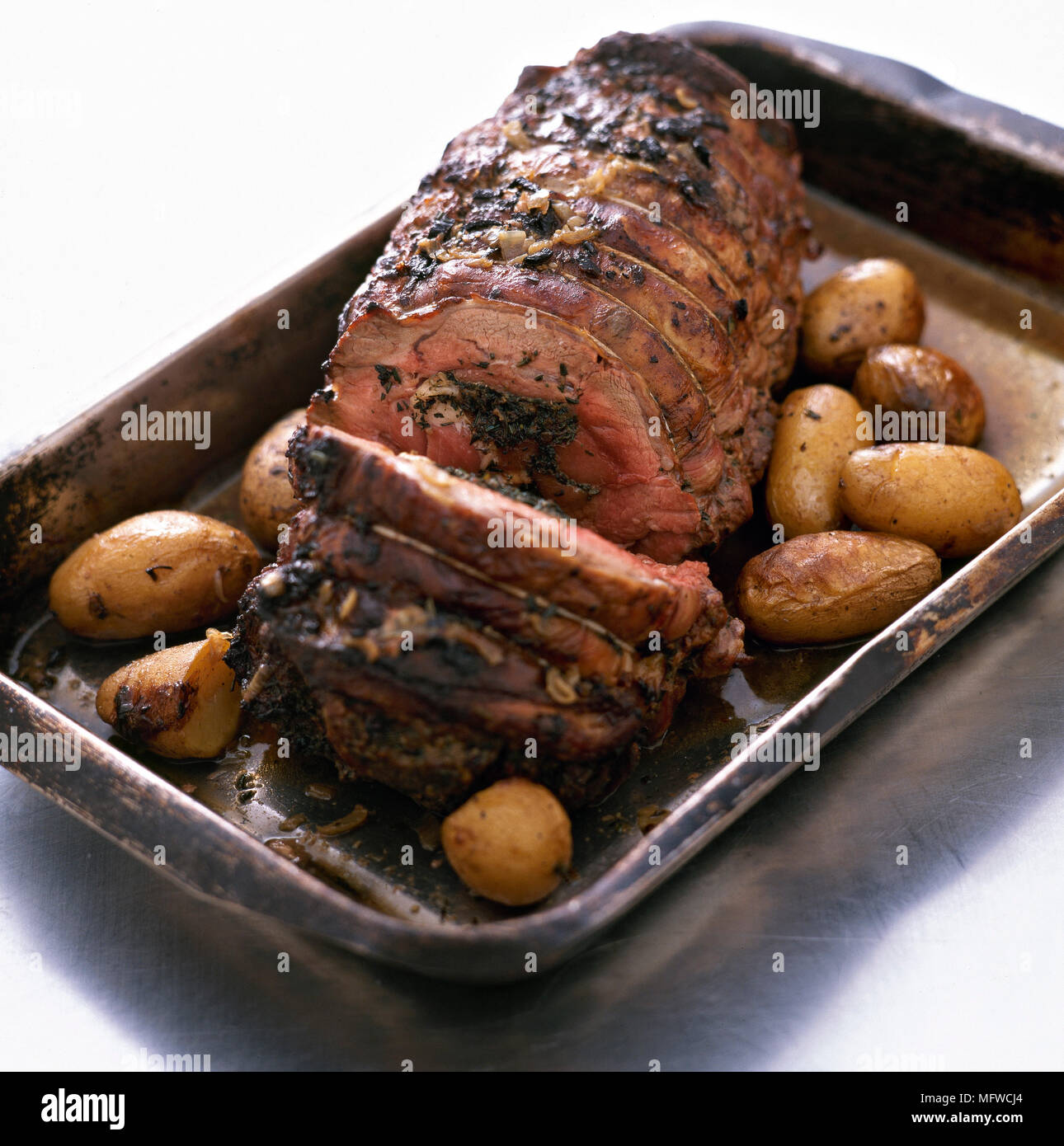 Roast beef joint and roast potatoes in roasting tin Stock Photo