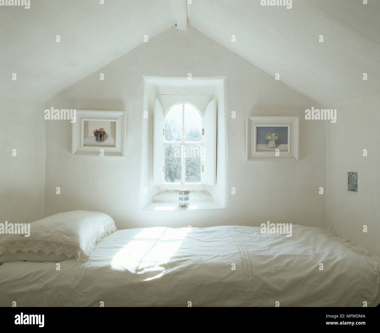 Simple white bedroom with single bed below window with shutters Stock