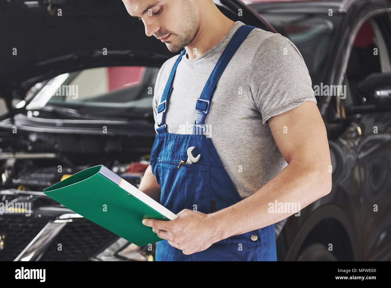 car service, repair, maintenance and people concept - auto mechanic man or smith with clipboard at workshop Stock Photo