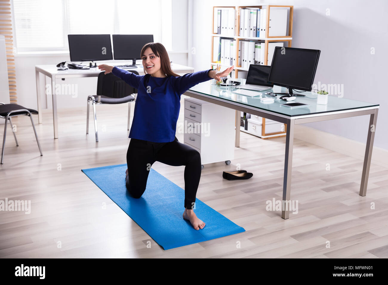 Side View Of A Young Businesswoman Doing Workout On Exercise Mat In Office Stock Photo