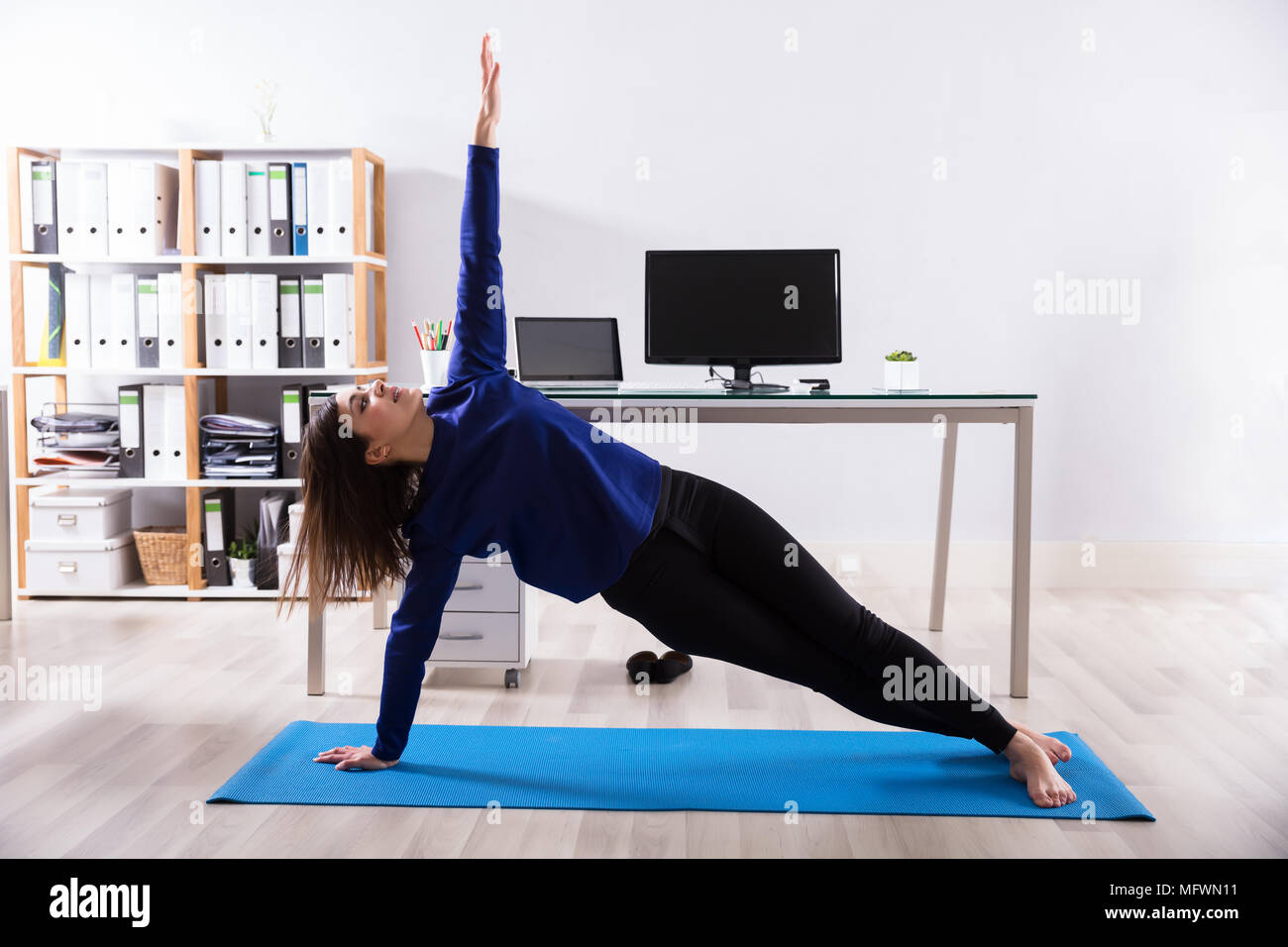 Young Businesswoman Doing Stretching Exercise On Exercise Mat At Workplace Stock Photo