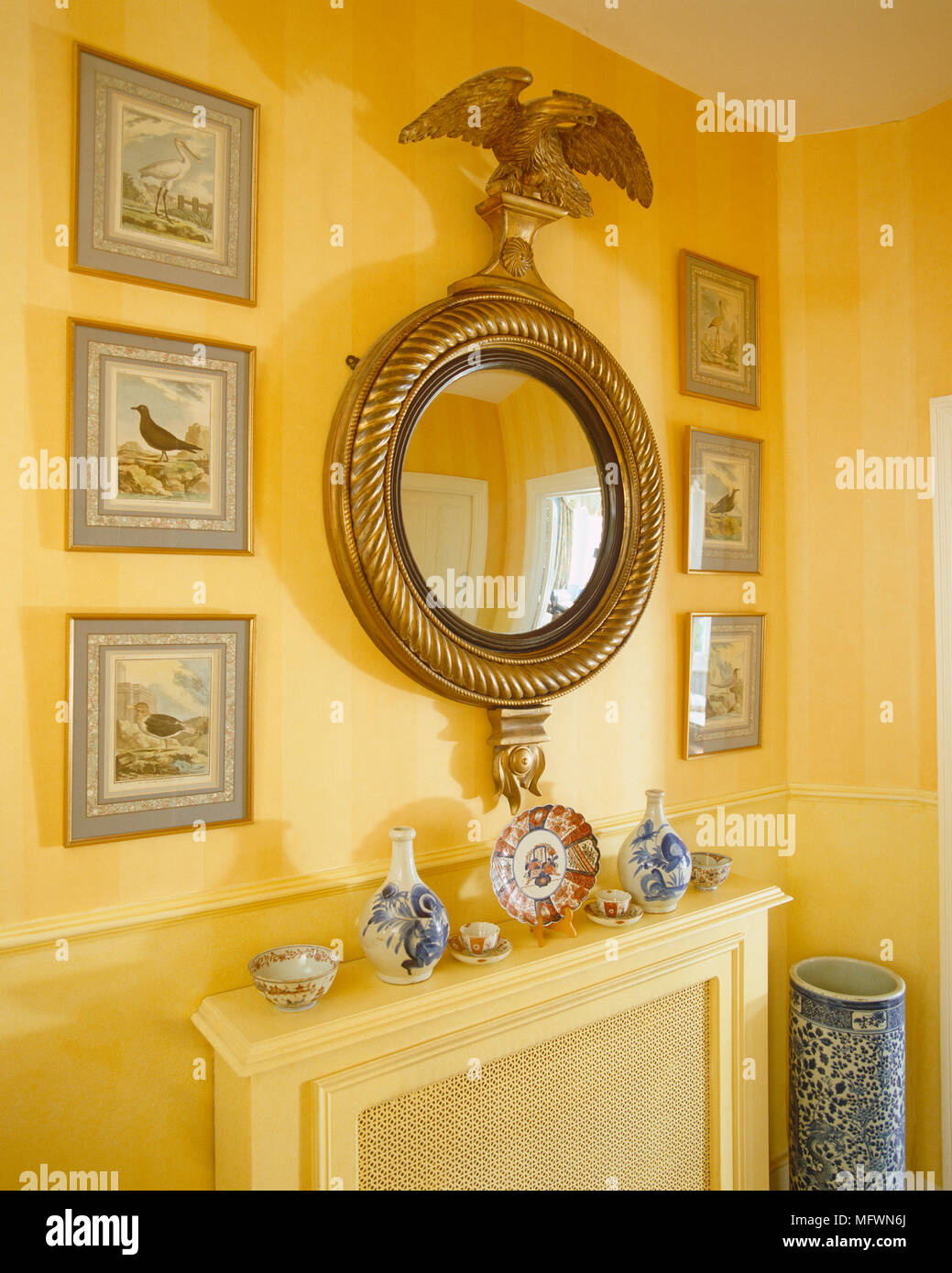 Ornate round gilt mirror above radiator cover on yellow wall Stock Photo