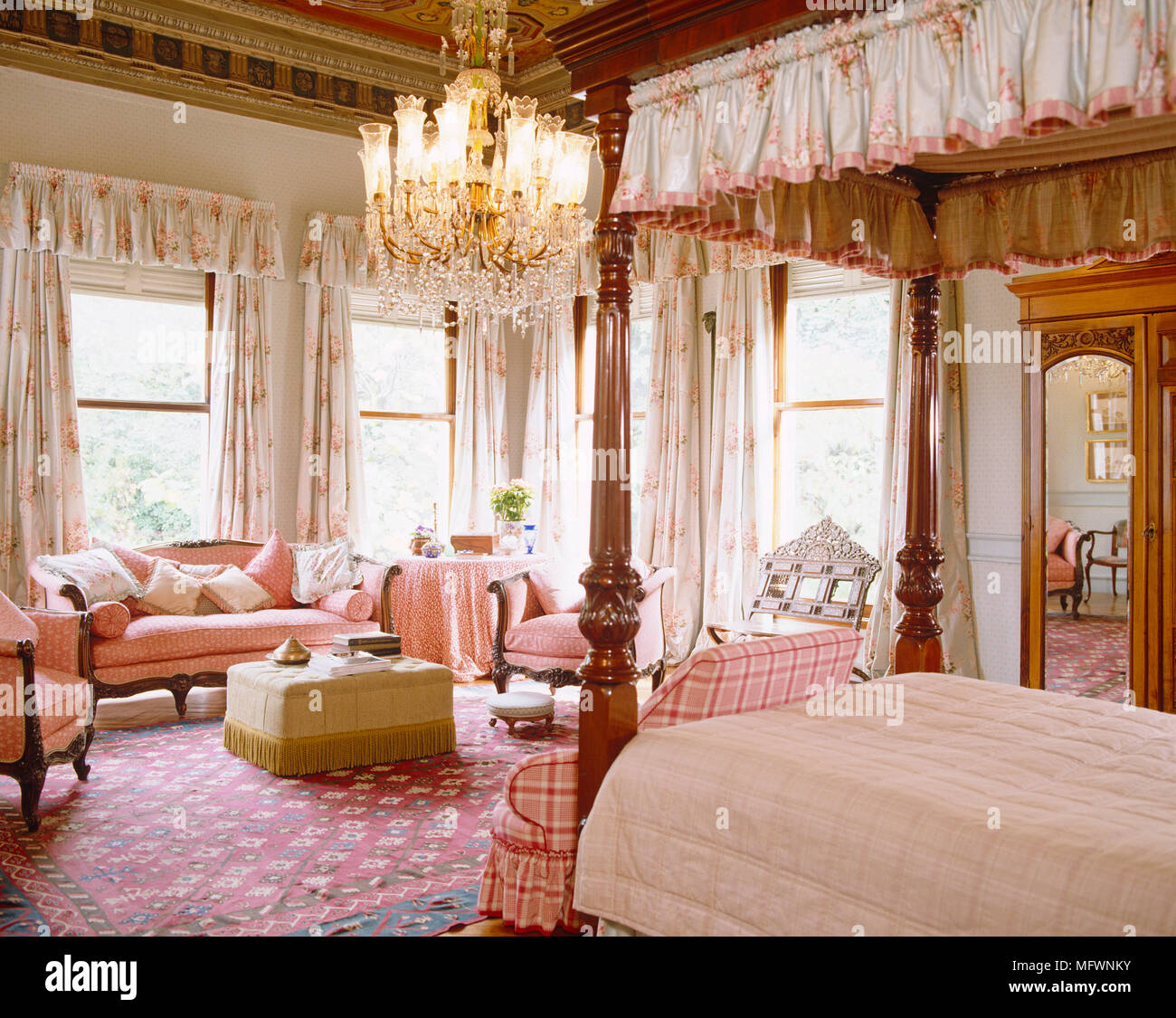 Wooden four poster bed with pink and white bed linen with sofa at end