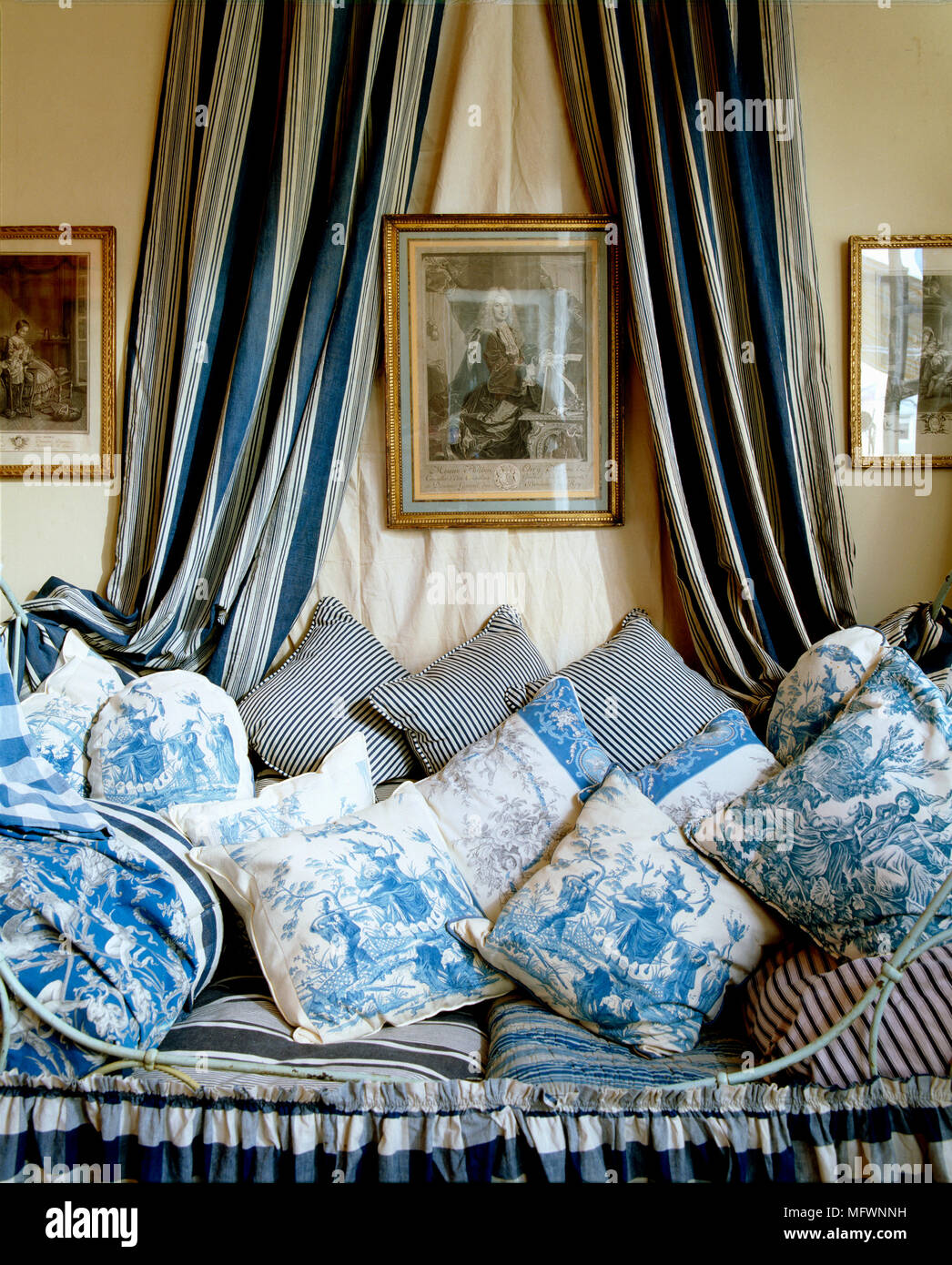 A detail of a grand, opulent bedroom, an antique metal framed bed with valance and blue and white striped drapes, pile of cushions covered in Toile de Stock Photo