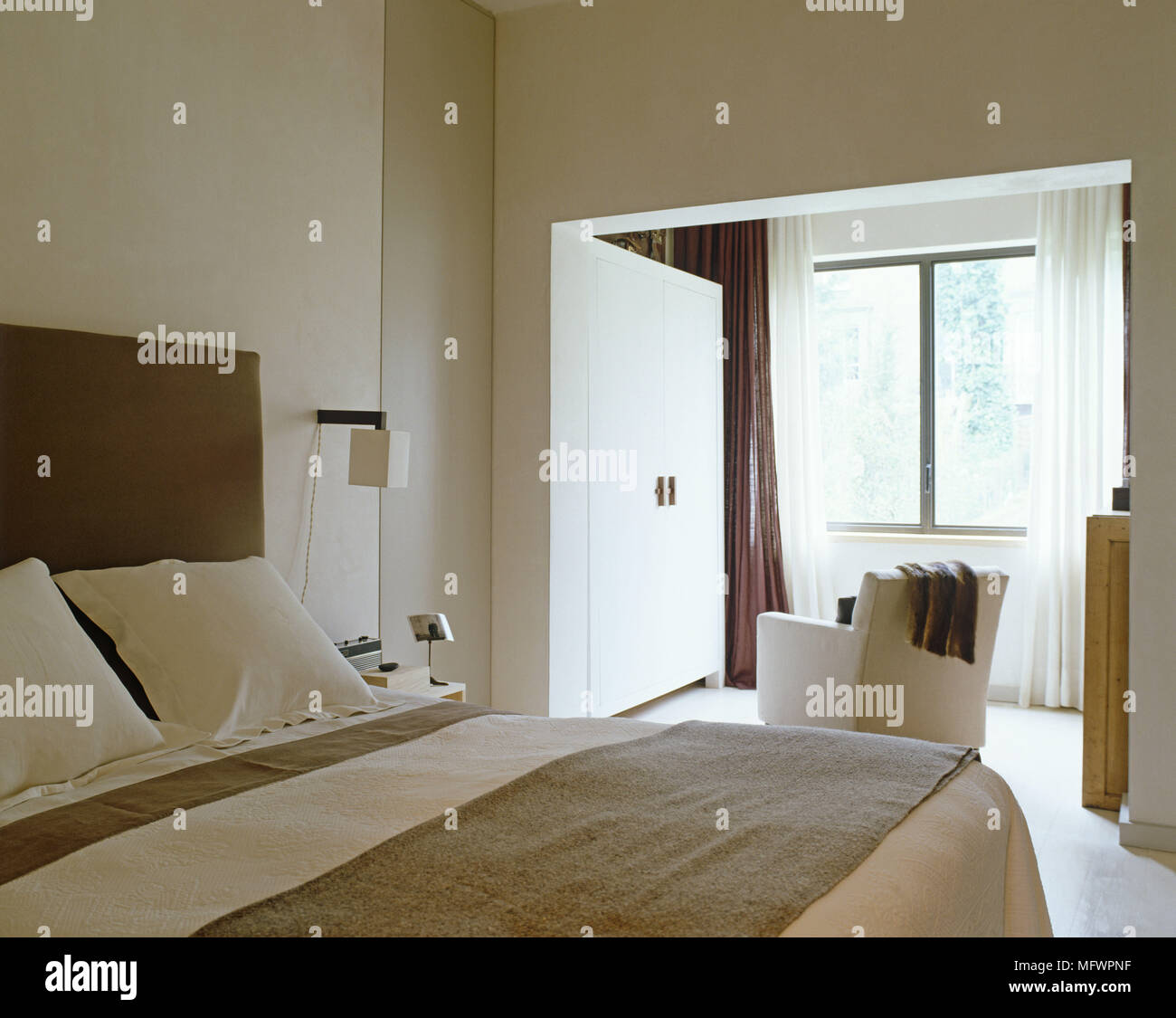 Minimalist bedroom with double bed with upholstered headboard next to alcove and armchair facing