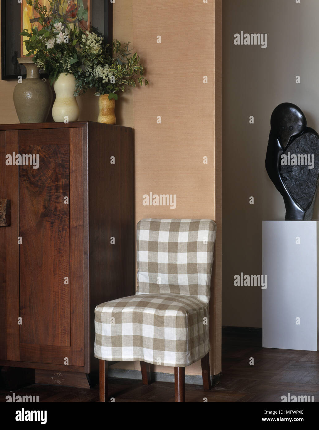 Chair With Checked Cover Next To Flowers On Top Of Wooden Cupboard