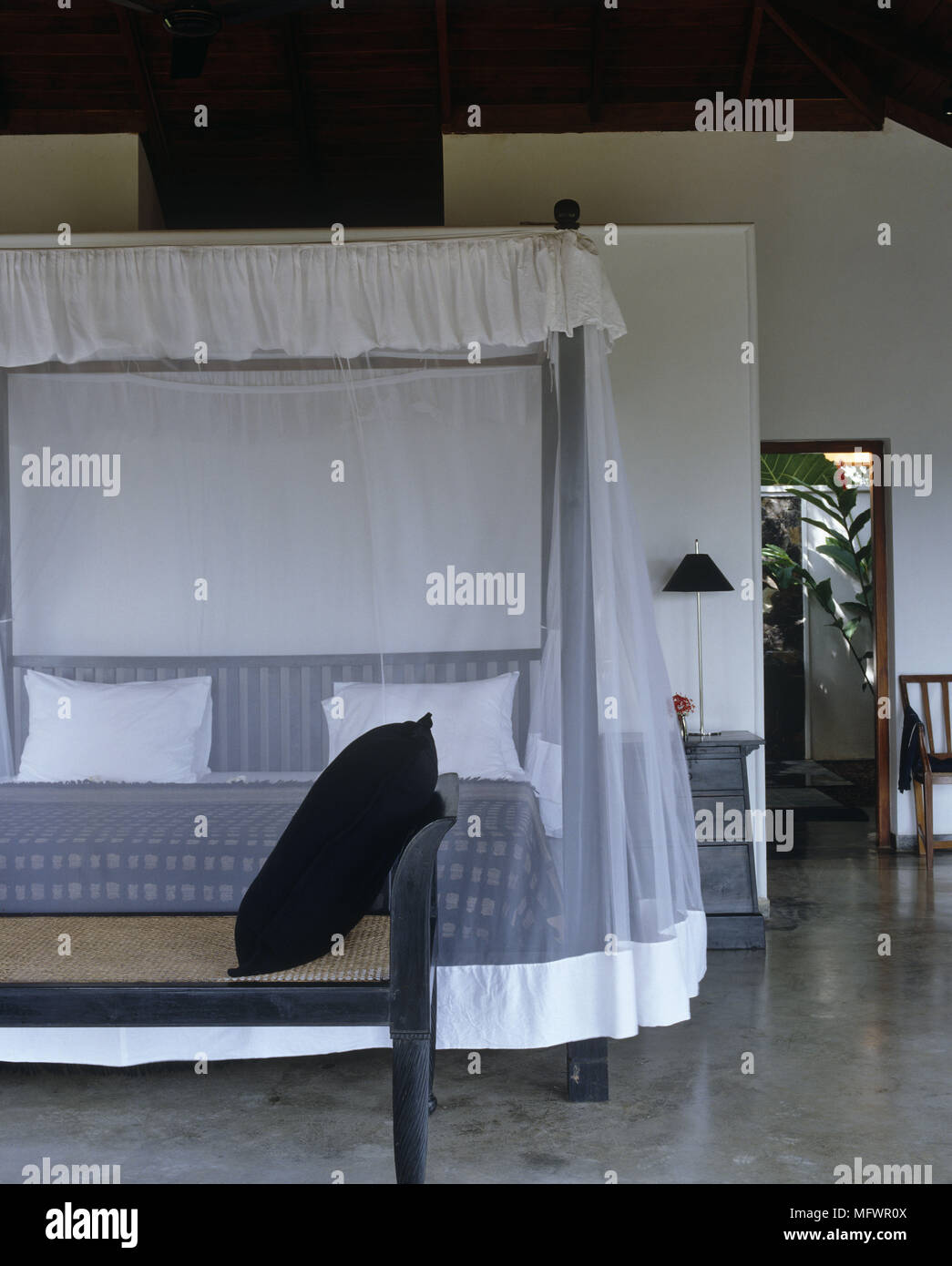 Cushion on seat in front of four poster bed with netting on concrete