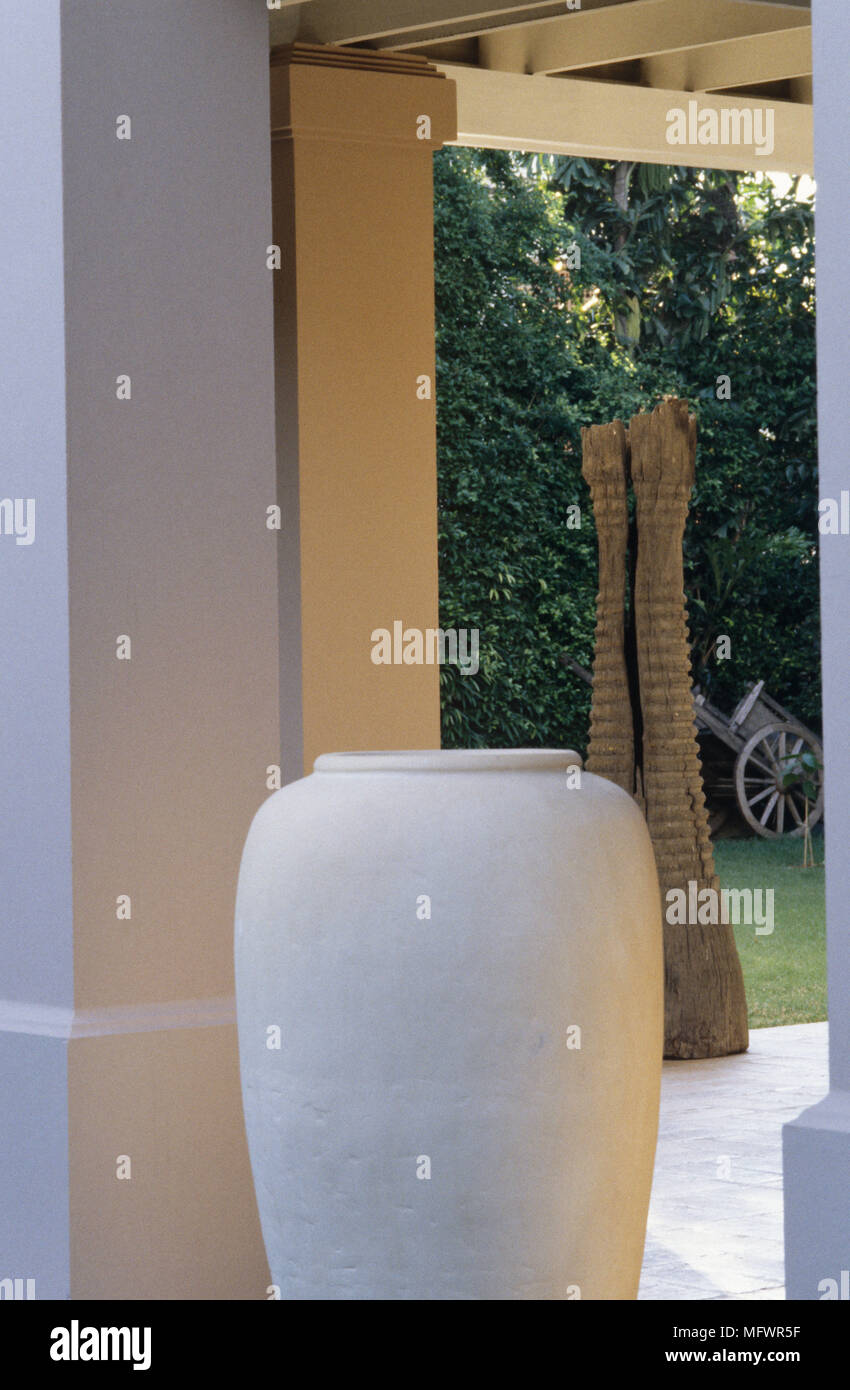 Large white vase in doorway leading out to garden patio with sculpture Stock Photo