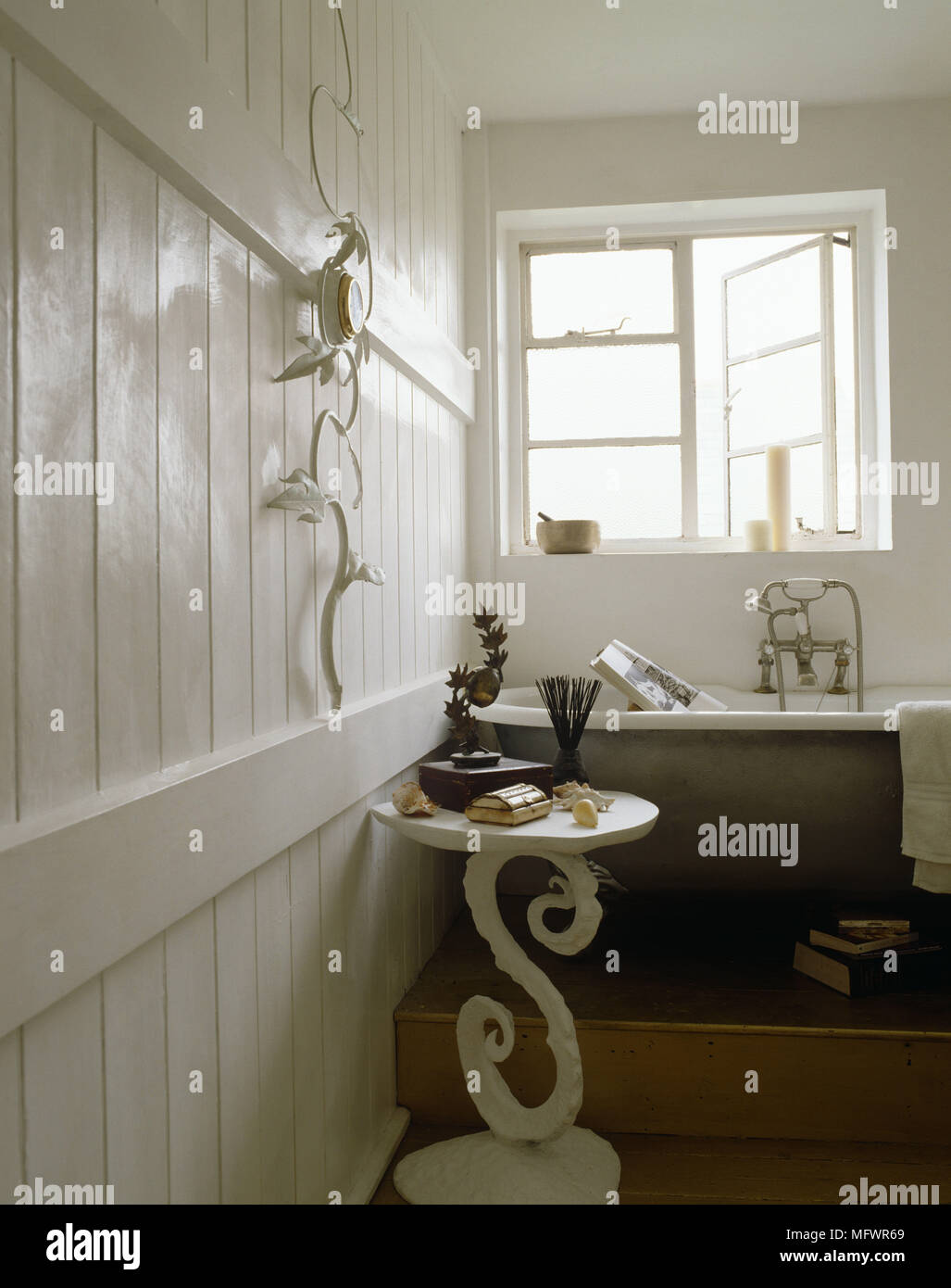 Bathroom with painted wood panelled wall and cast iron bath on raised platform next to window Stock Photo