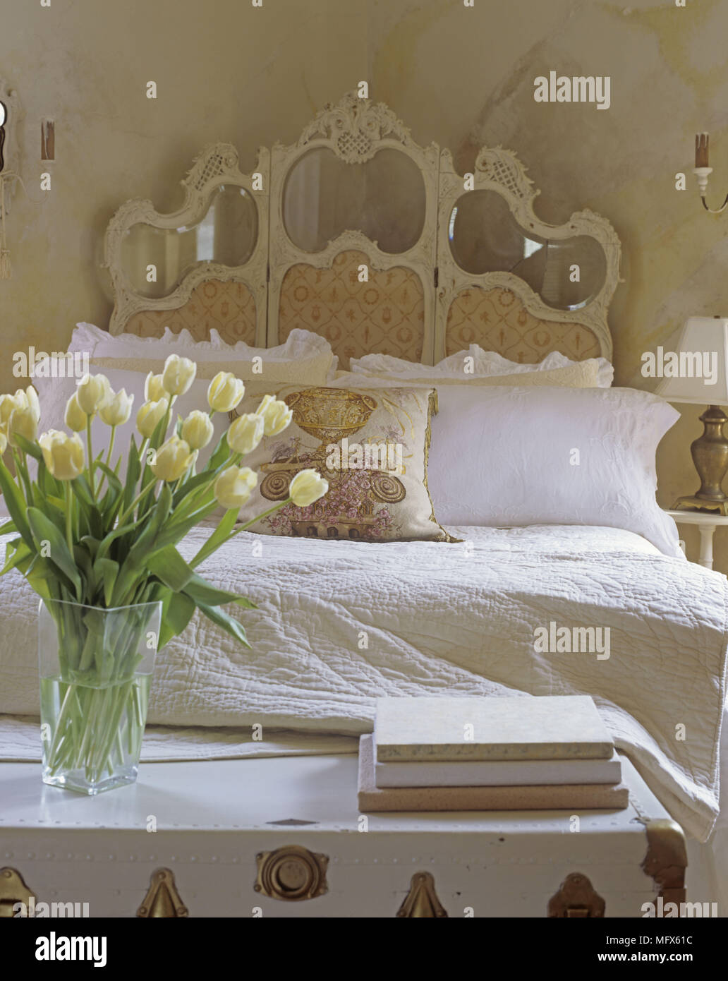A traditional bedroom with a double bed white chest and changing screen flower arrangement of yellow tulips Stock Photo