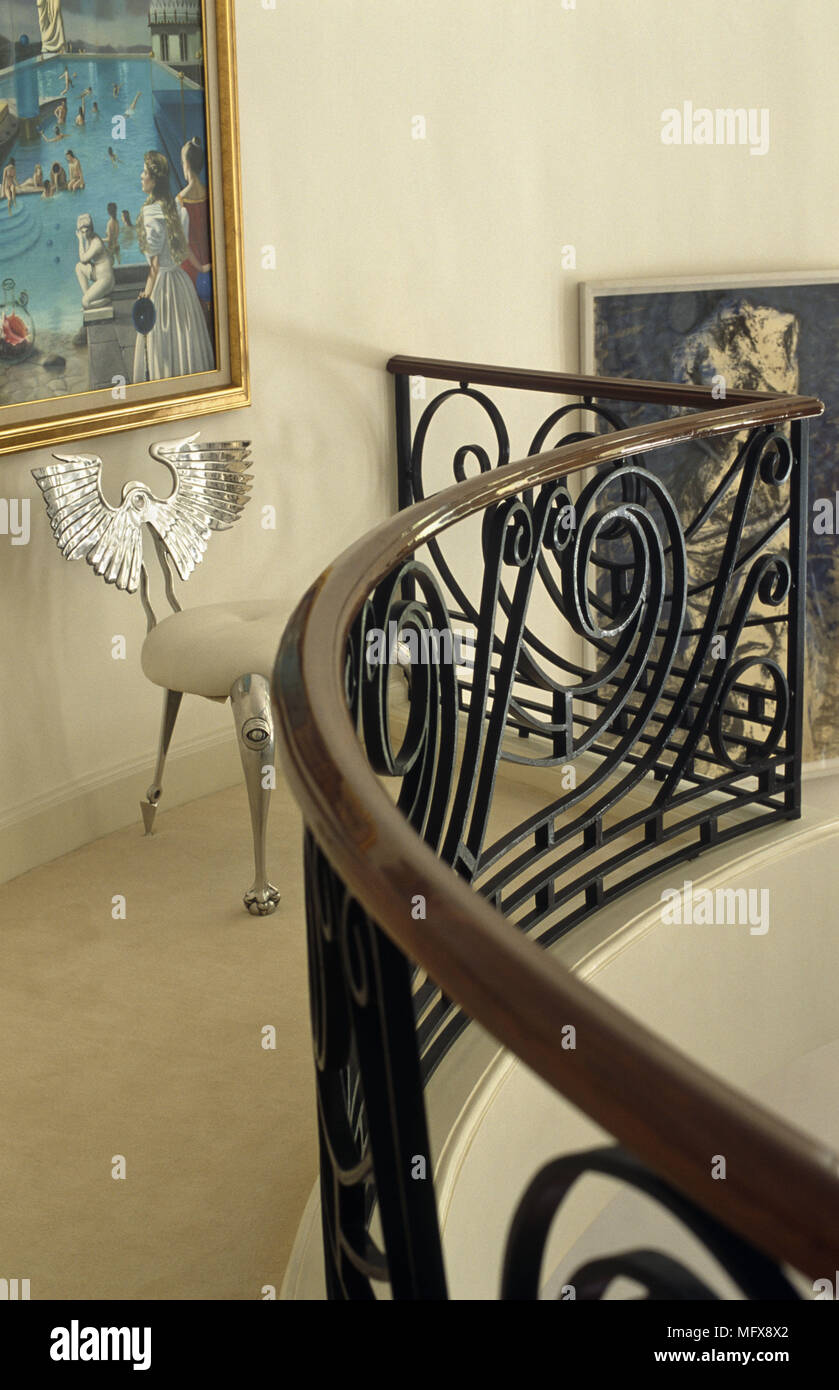 Ornate silver chair on landing area with curving wrought iron and wooden banister Stock Photo