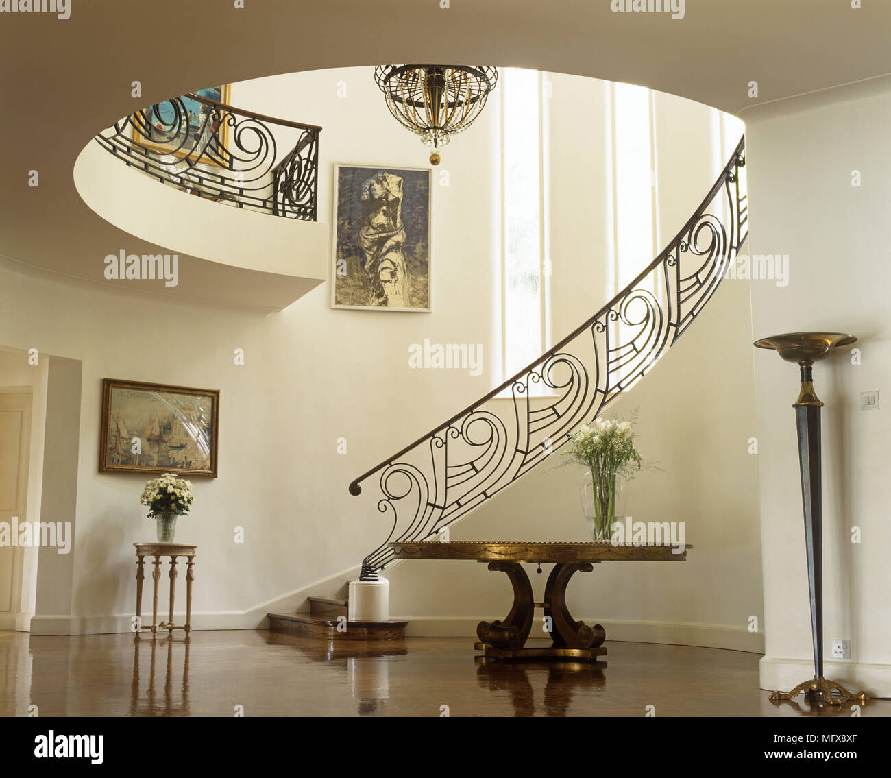 Pedestal table in hallway with elegant curving staircase behind Stock