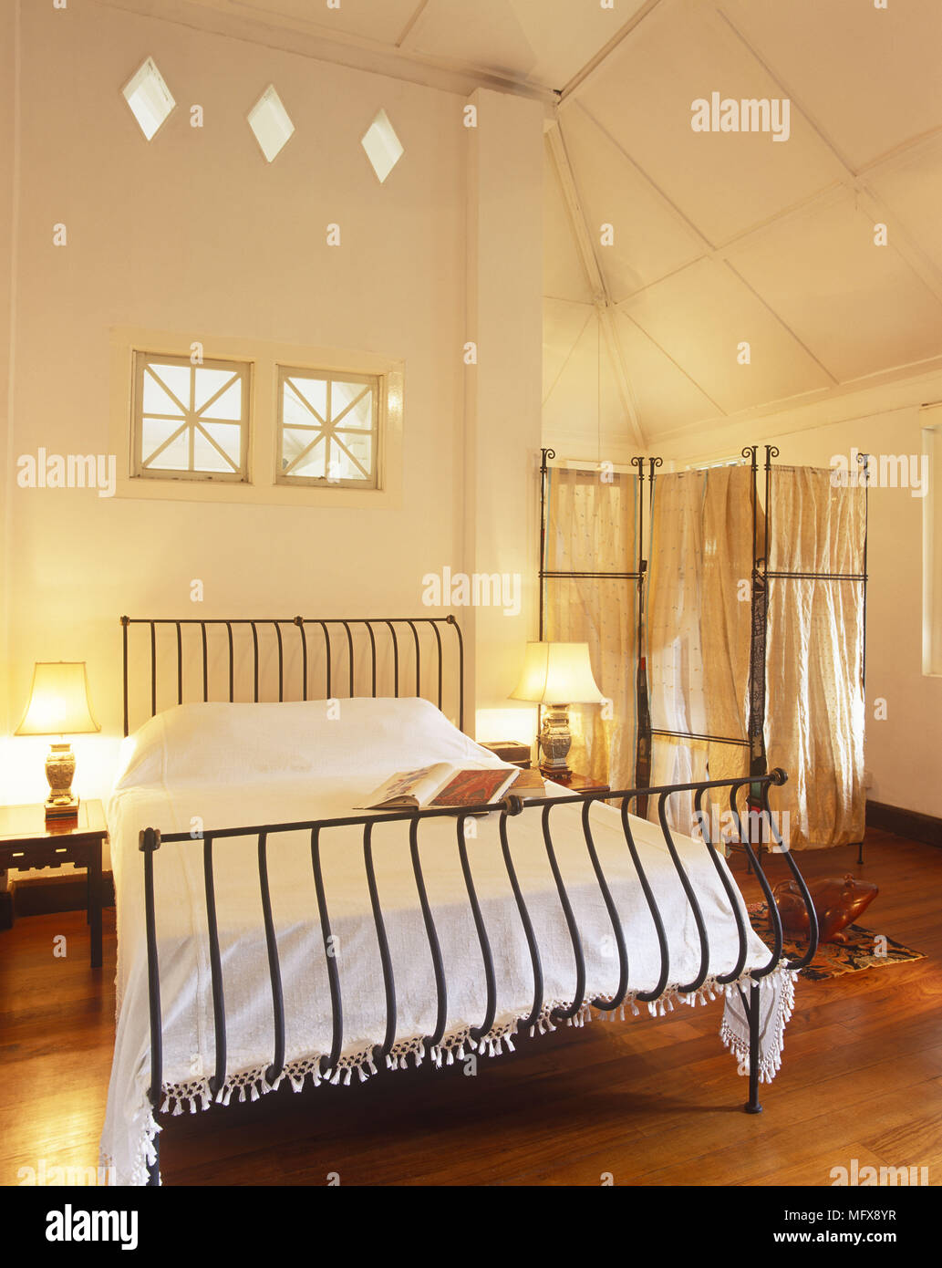 Lit Lamps On Bedside Tables Either Side Of Wrought Iron