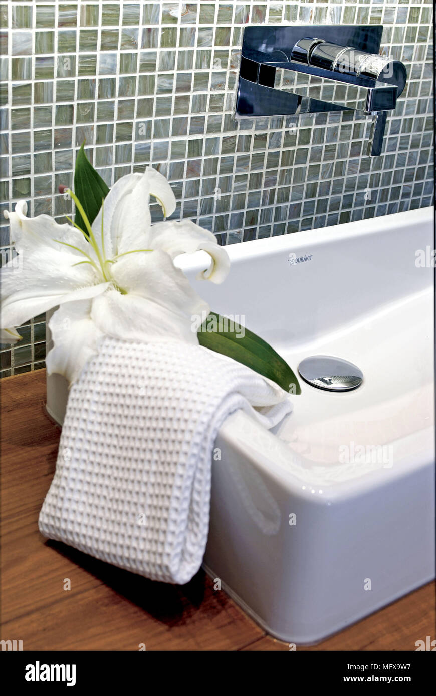 Cotton towel and lily flower draped over washbasin on wooden shelf Stock Photo