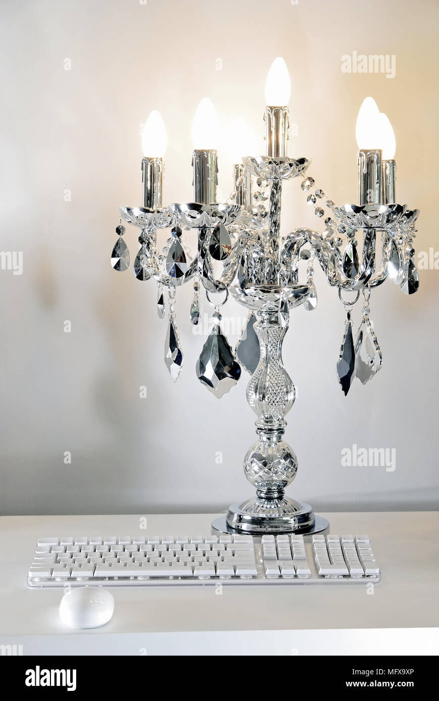 Glass and silver candelabra behind computer keyboard and mouse Stock Photo