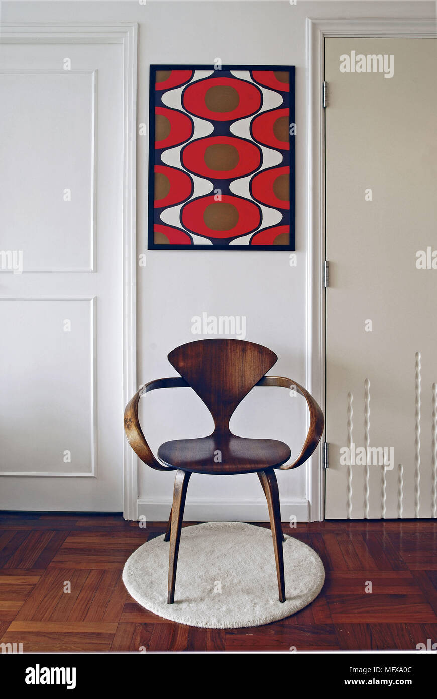 Red abstract artwork above wooden chair set on round mat Stock Photo ...
