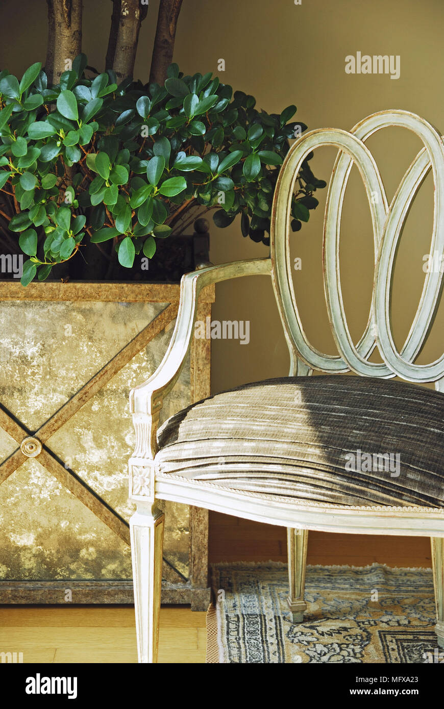 Period style armchair in front of tree in gold planter Stock Photo