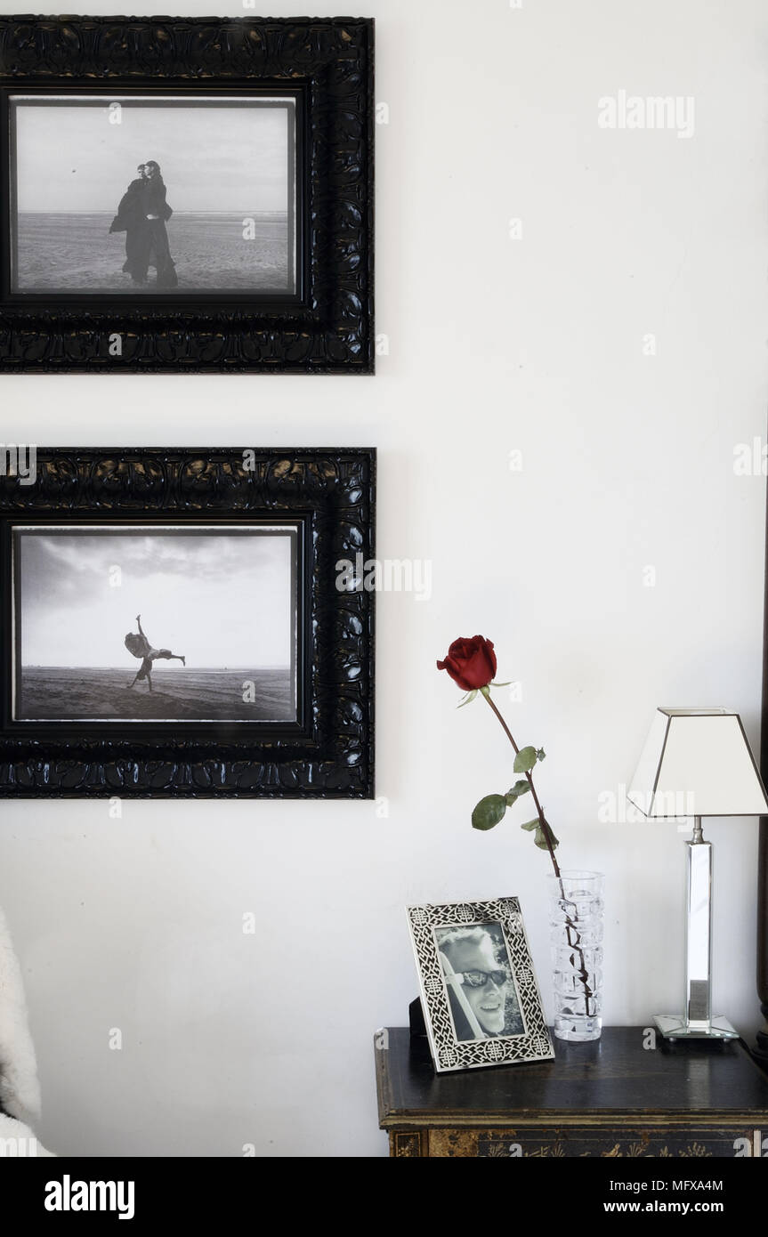 Lamp and single rose on wooden table with framed photographs above Stock Photo