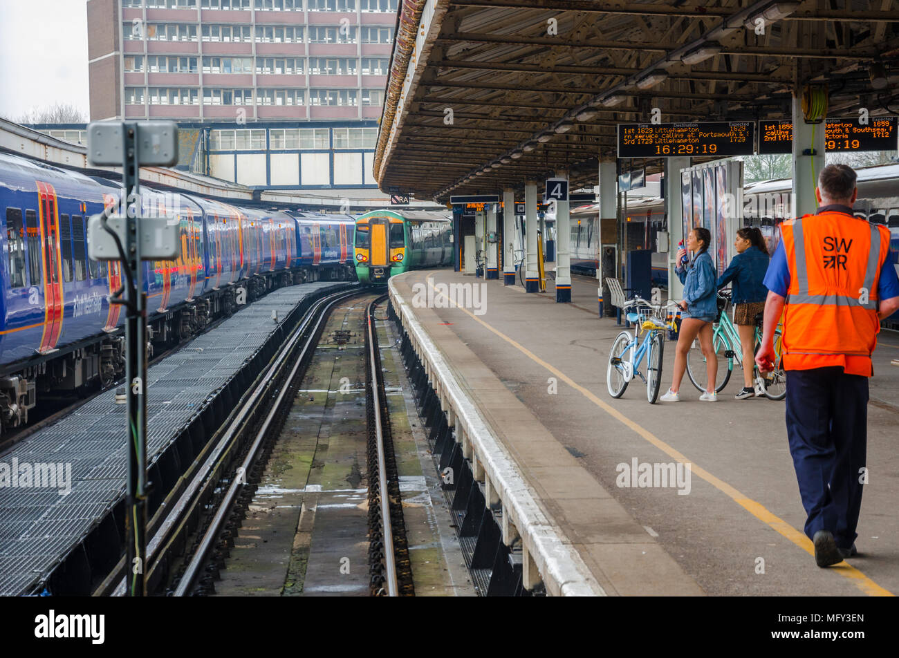 Two ladies with bicycles wait on the platform at Portsmouth Harbour Railway Station as a train  departs. Stock Photo
