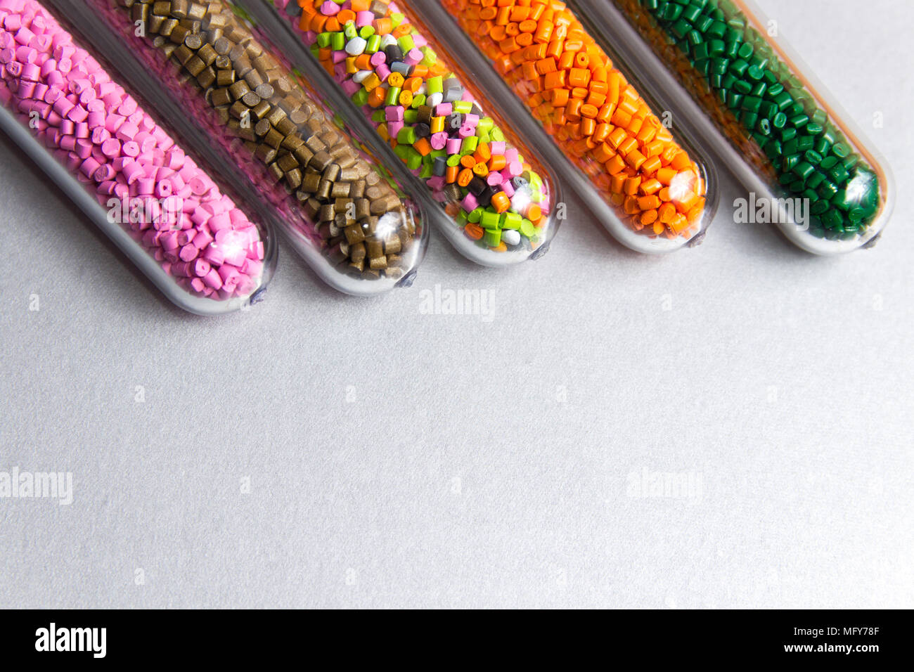Plastic pellets .Polymeric dye in test tubes on gray background. Plastic granules after processing of waste polyethylene and polypropylene. Stock Photo