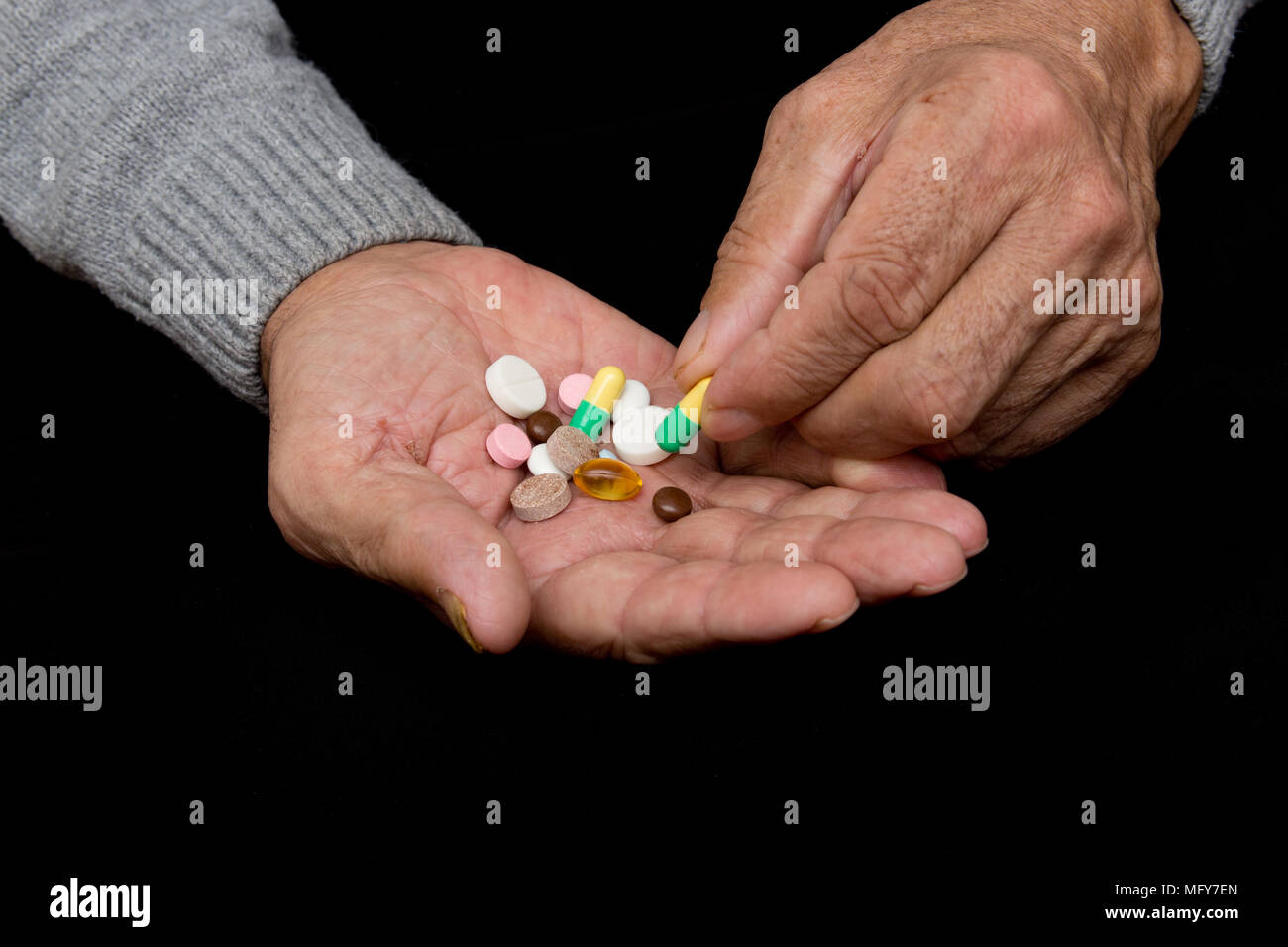 An elderly man holds a lot of colored pills in old hands. Painful old
