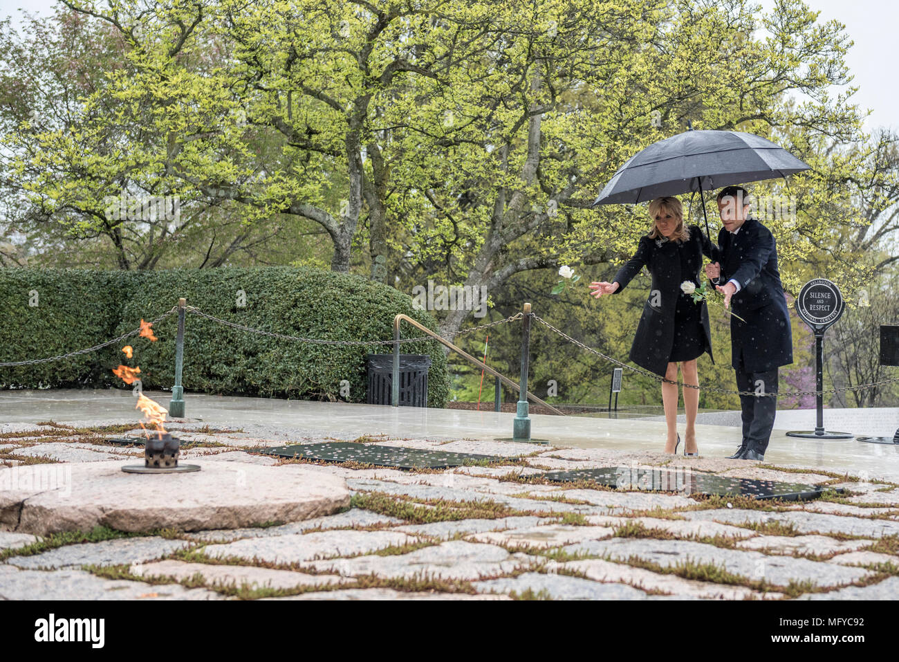 French President Emmanuel Macron, right, and his wife Brigitte Macron, place single white roses on the gravesite of former President John F. Kennedy and Jacqueline Bouvier Kennedy Onassis on a rainy day at Arlington National Cemetery April 24, 2018 in Arlington, Virginia. Stock Photo