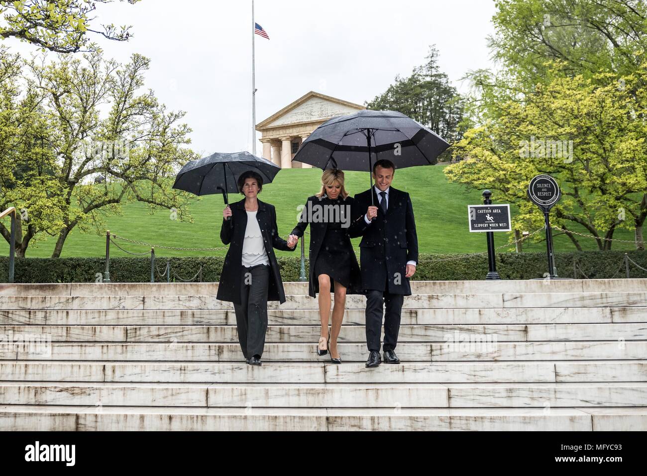 French President Emmanuel Macron, right, and his wife Brigitte Macron, are escorted by superintendent Katharine Kelley, left, during a visit to the gravesite of former President John F. Kennedy and Jacqueline Bouvier Kennedy Onassis on a rainy day at Arlington National Cemetery April 24, 2018 in Arlington, Virginia. Stock Photo